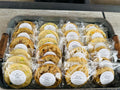 Tray of assorted cookies in clear packaging with labels on a wooden surface.